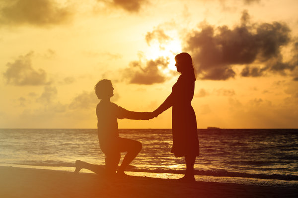 Silhouette of romantic couple at sunset beach, marriage proposal