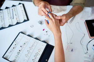 Closeup of man checking ring size of elegant female hand in custom jewelry shop